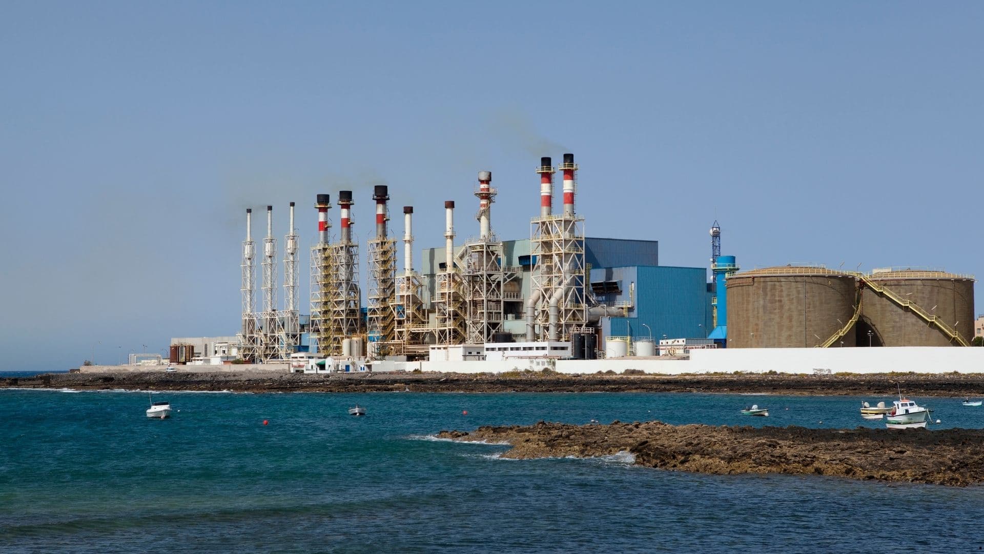 Coastal desalination and power plant with exhaust stacks beside the sea.